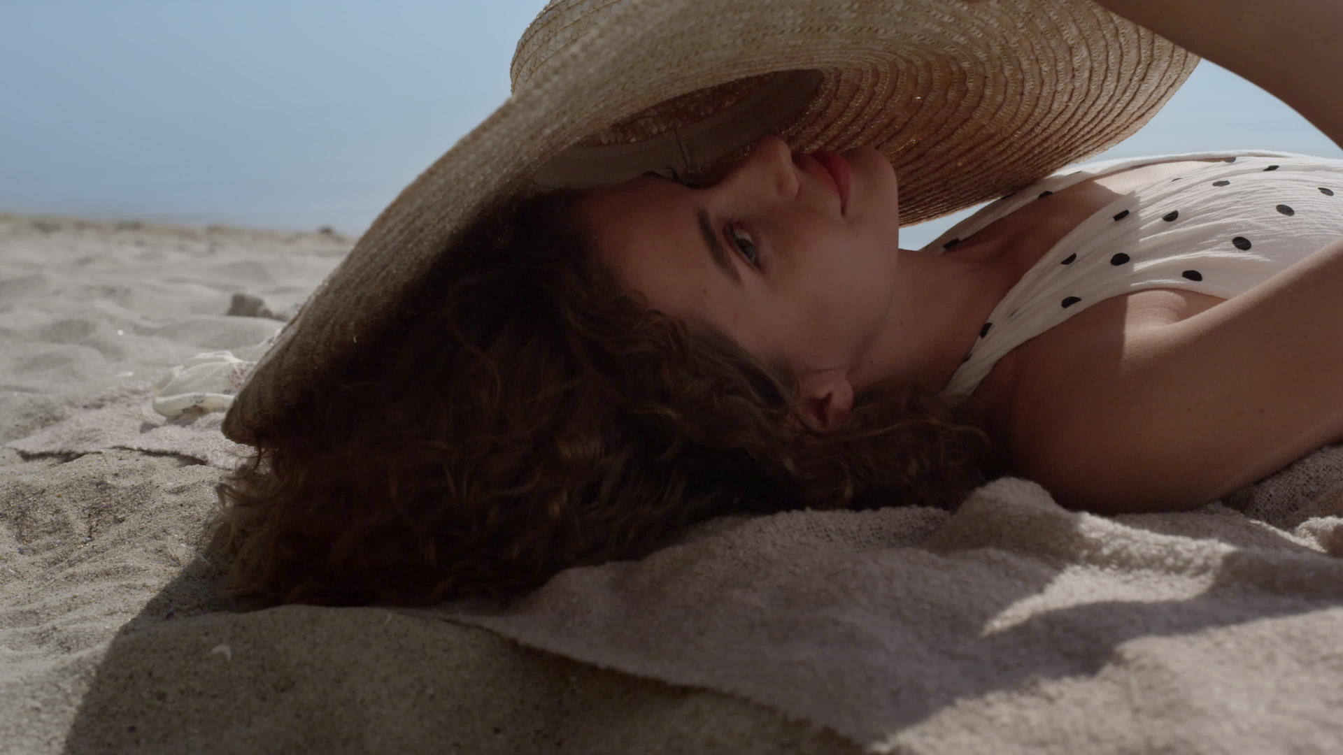 快乐的笑容女孩从躺在沙滩上的宽边帽中望去视频的预览图