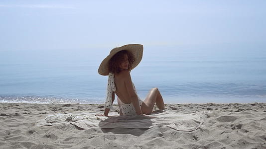 时髦的女人回头坐在阳光明媚的海边视频的预览图