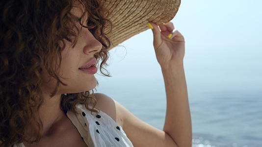 一位身穿宽边草帽的豪华女子在阳光明媚的沙滩上视频的预览图