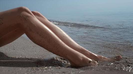 晒黑的女人的腿在阳光特写上涂上了沙滩和沙子视频的预览图