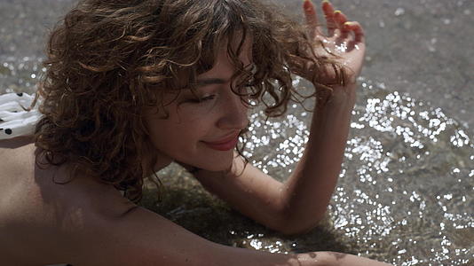 一个放松的女孩躺在海水里触摸湿沙特写视频的预览图