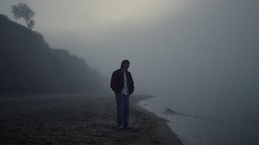 轻松的人耳机站在雾蒙蒙的沙滩上视频的预览图