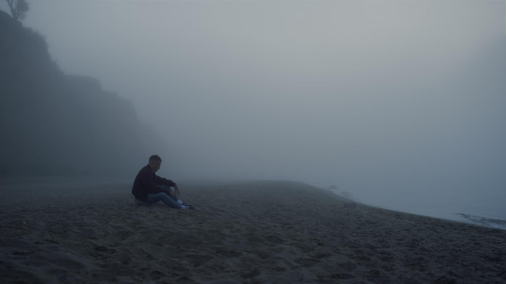 早晨在雾中坐在海边的沮丧的人视频的预览图