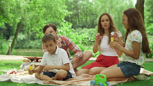 四口之家坐在树林餐布上享受野餐的快乐时光视频的预览图