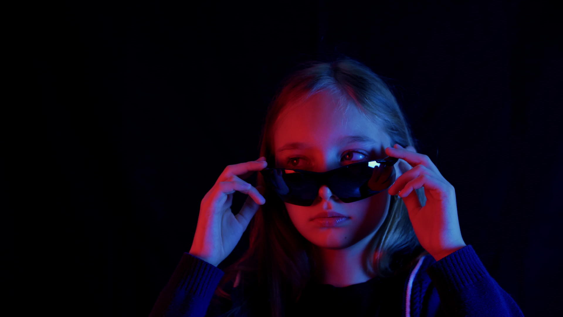 那个戴着黑色太阳镜的女孩在黑暗的房间里看着红光和蓝光视频的预览图