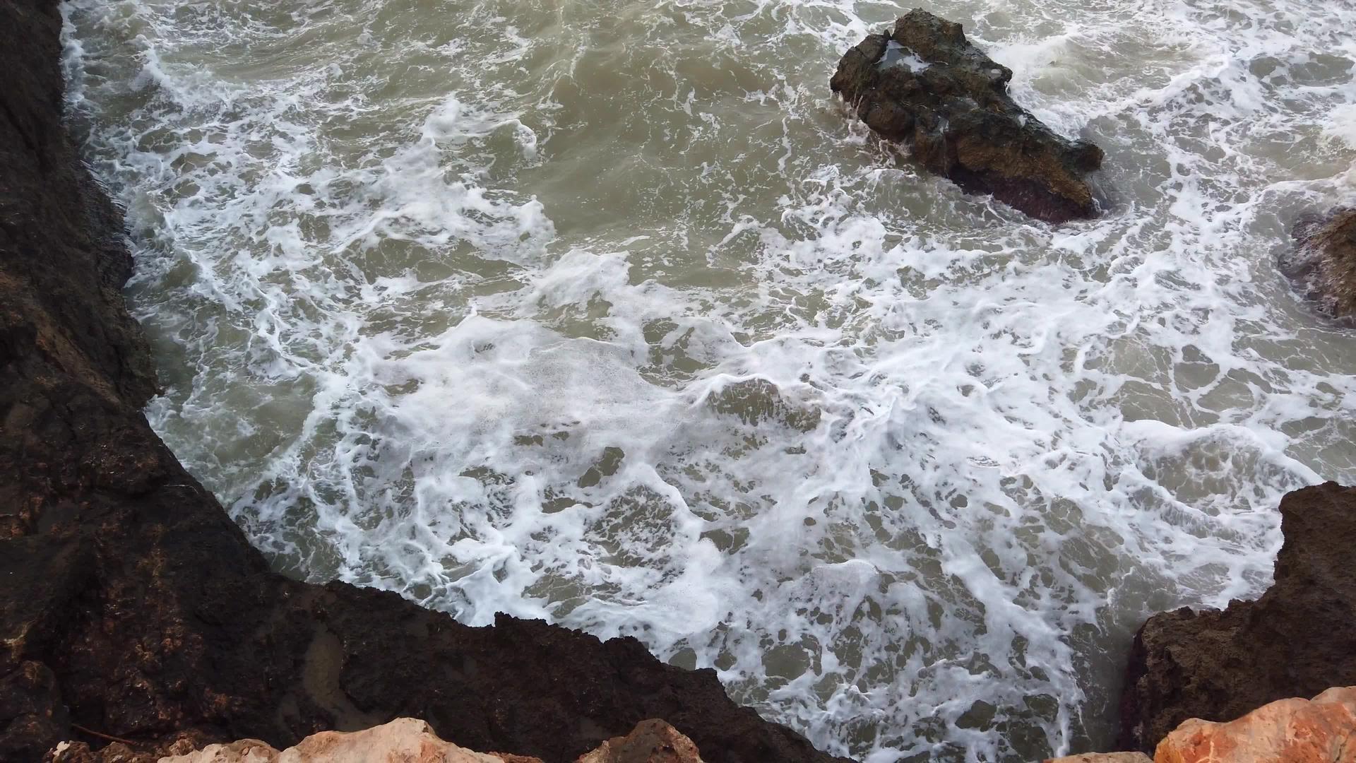 大浪撞击岩石高高的岩石在沙滩上大量的白色泡沫在暴风雨中视频的预览图