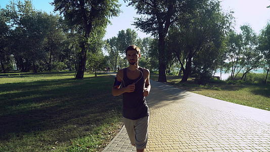 一个戴着耳机的年轻人在公园里跑回来在那里散步和跑步视频的预览图