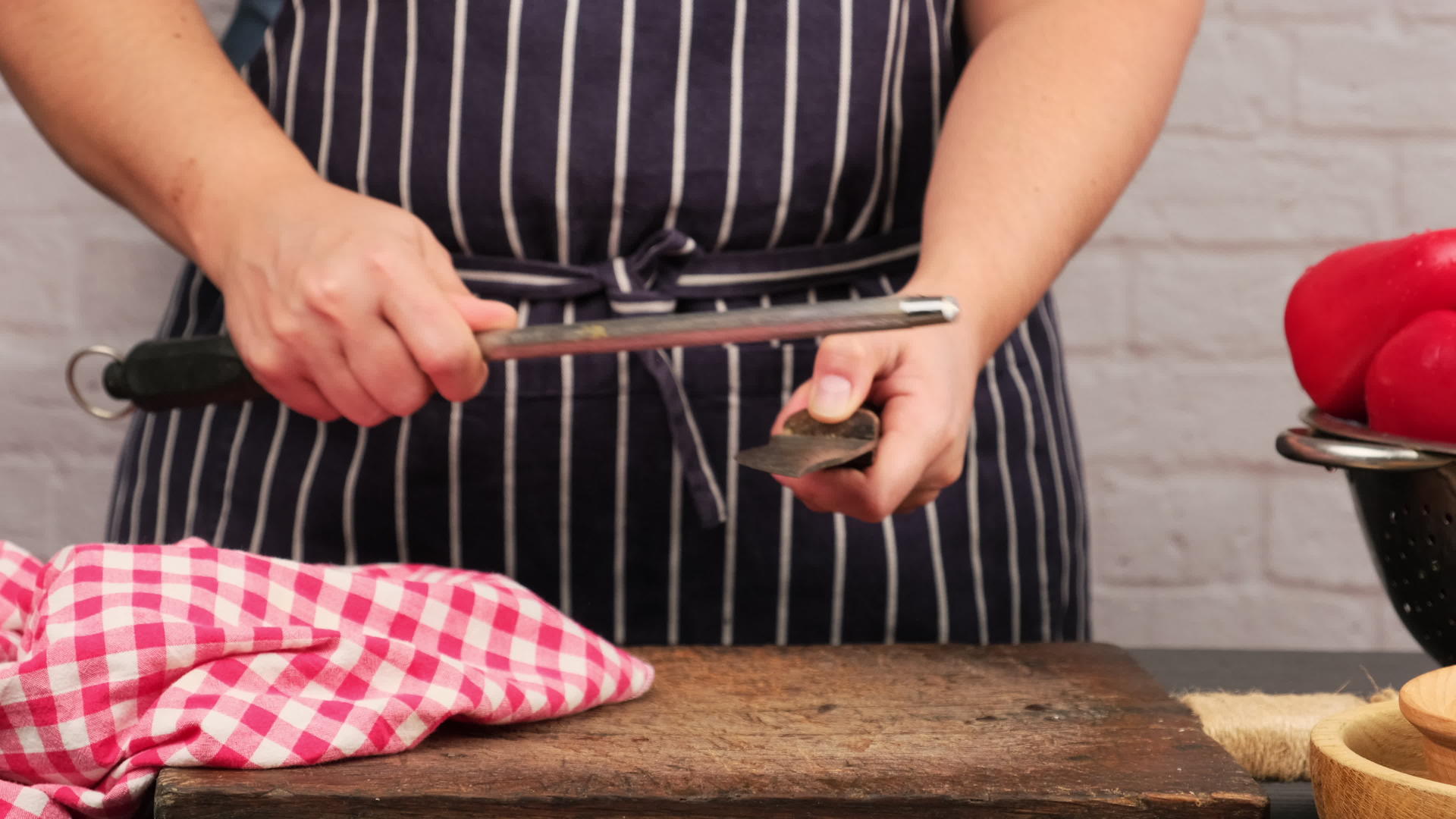 穿蓝色围裙的女人用刀在桌子上磨厨房刀和手柄视频的预览图