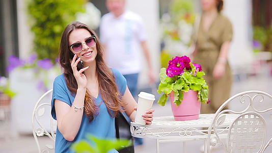 在露天咖啡馆购物喝咖啡后时尚快乐的女孩通过电话交谈视频的预览图