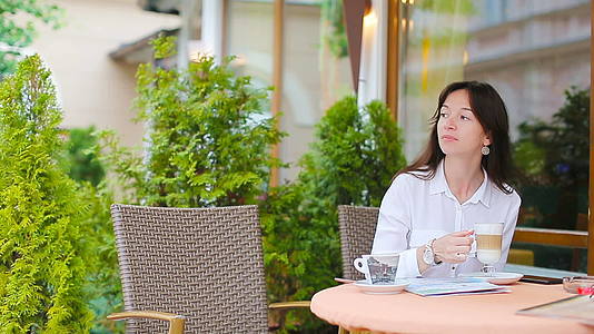 美丽的女人坐在户外咖啡馆喝咖啡用智能手机画像视频的预览图