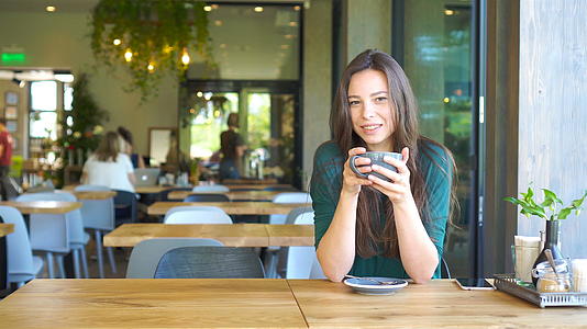 坐在户外咖啡馆喝咖啡的年轻女性用咖啡为快乐女孩画像视频的预览图