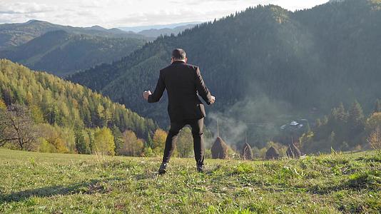 一个穿着黑色西装的男人在一座美丽的山上玩得很开心视频的预览图