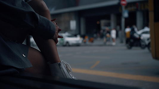 妇女的腿坐在城市背景下拥挤的街道附近的公共汽车站上视频的预览图