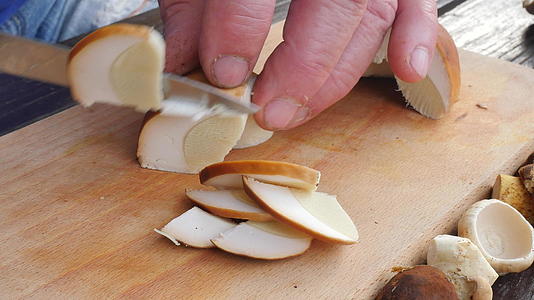 美丽的野生蘑菇在木制砧板上用刀切成小块男人的手在木桌上视频的预览图