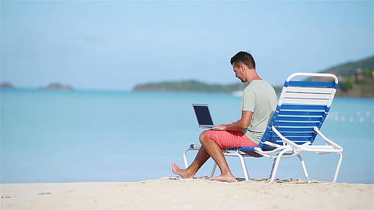在热带沙滩度假期间年轻男子带着平板电脑视频的预览图