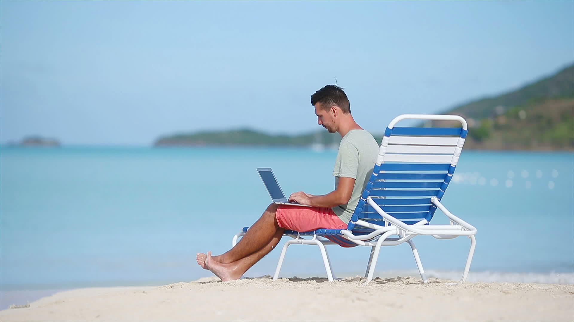 年轻男子在热带加勒比海滩上带着笔记本电脑视频的预览图