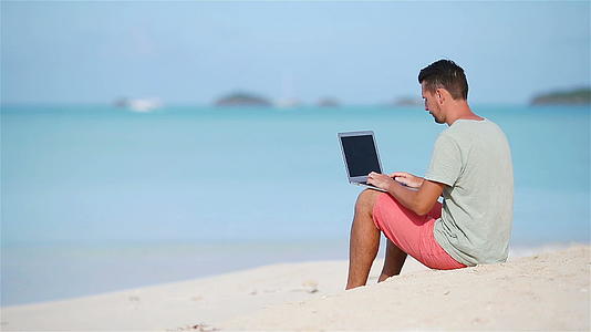 在热带沙滩度假期间年轻男子带着平板电脑视频的预览图