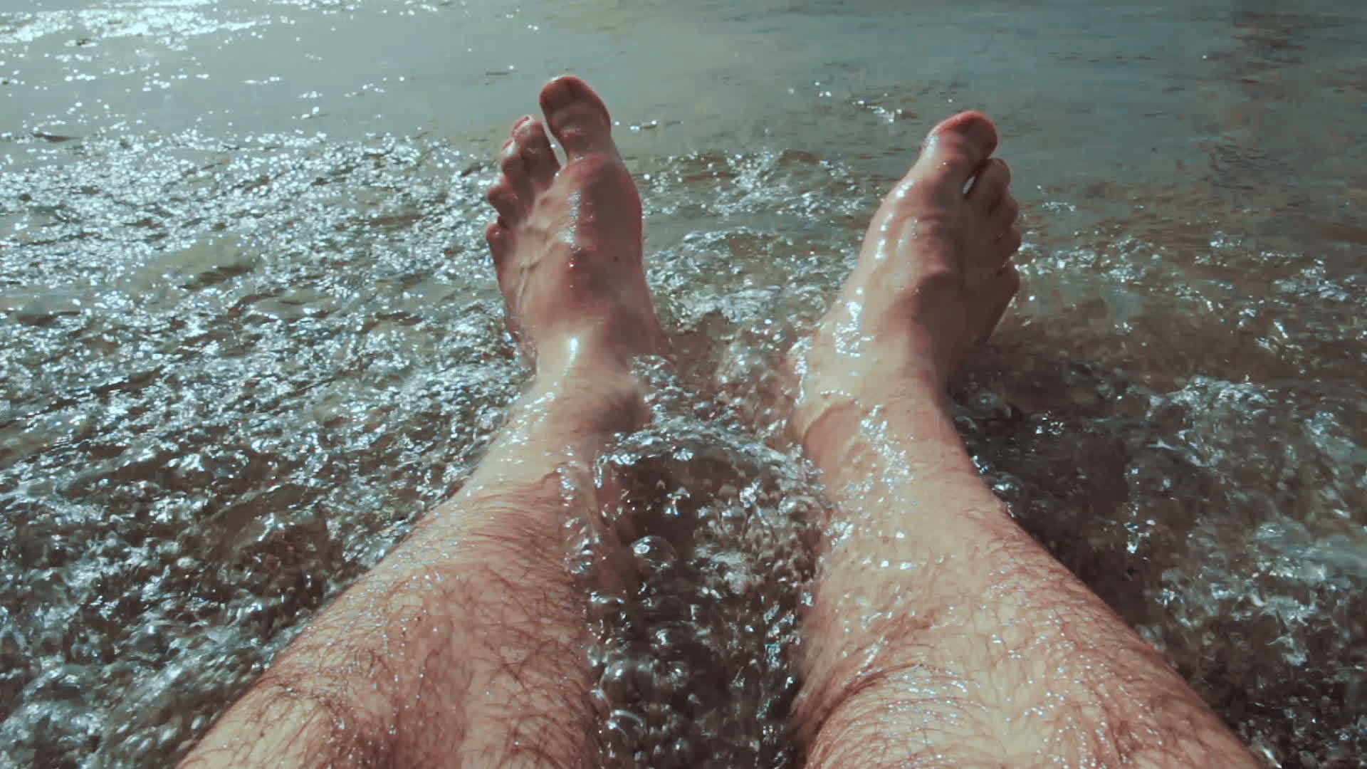 一个白人男子坐在水里他的腿被海滩上的海浪冲视频的预览图