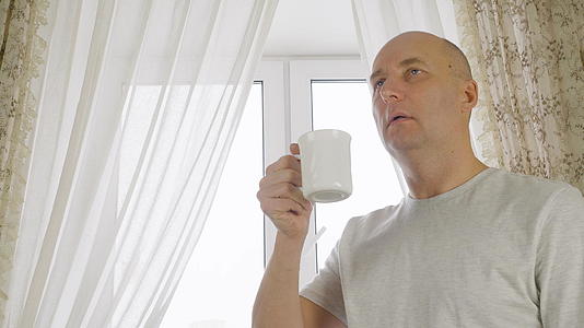 成年男子在以窗户为背景的舒适厨房里喝咖啡早晨的咖啡肖像令人愉快视频的预览图