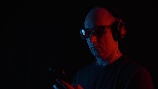 成年男子用耳机在黑色背景上听移动音乐视频的预览图