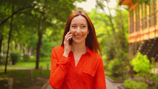 一个微笑的年轻女子在城市公园里通过电话走过视频的预览图