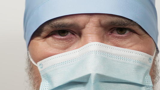 医生戴着一次性医用口罩和白色背景蓝色纺织帽看着镜头视频的预览图