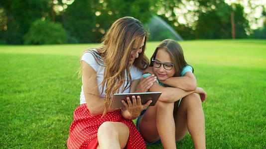 女儿和母亲在草坪上使用平板电脑视频的预览图