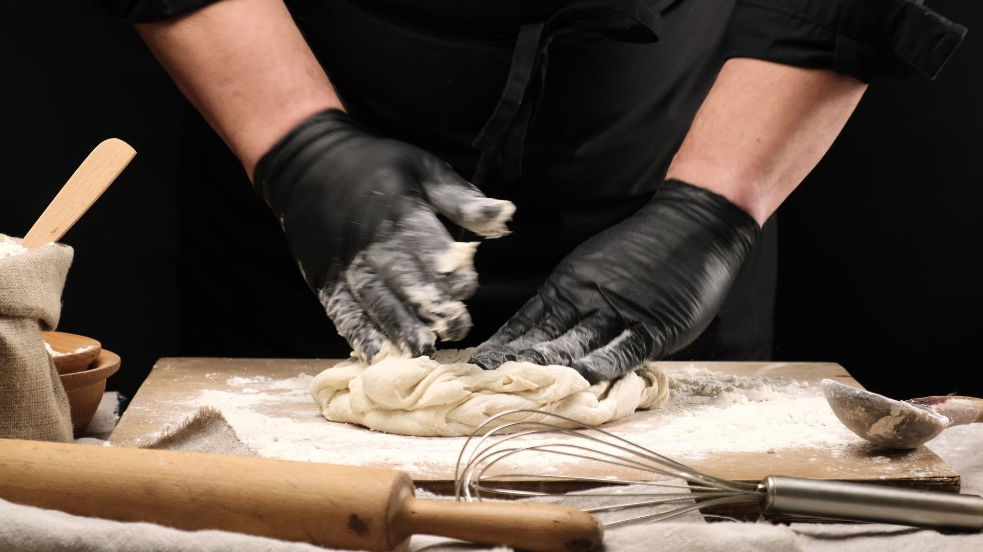 黑色乳头厨师用黑色面粉手套在木板上喷上白色小麦粉面团视频的预览图