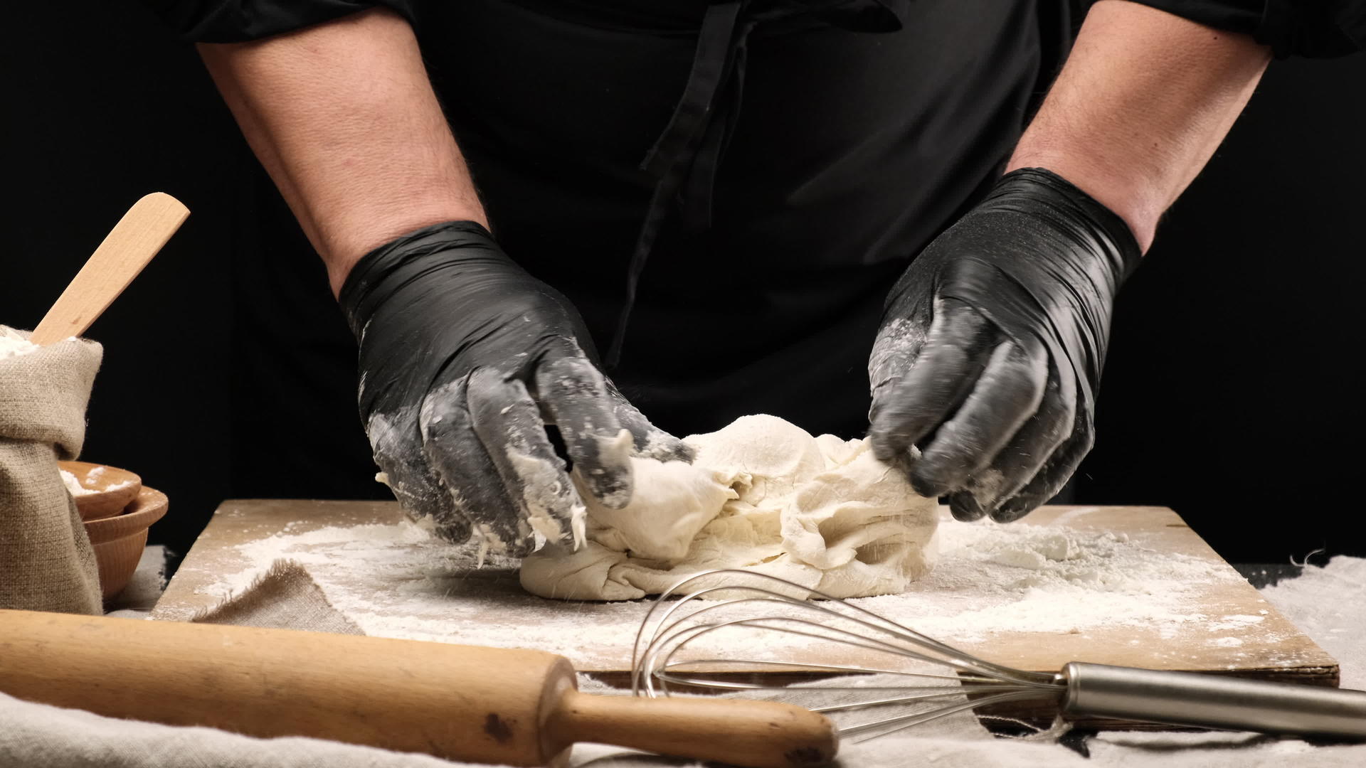 黑色乳头厨师用黑色面粉手套在木板上喷上白色小麦粉面团视频的预览图