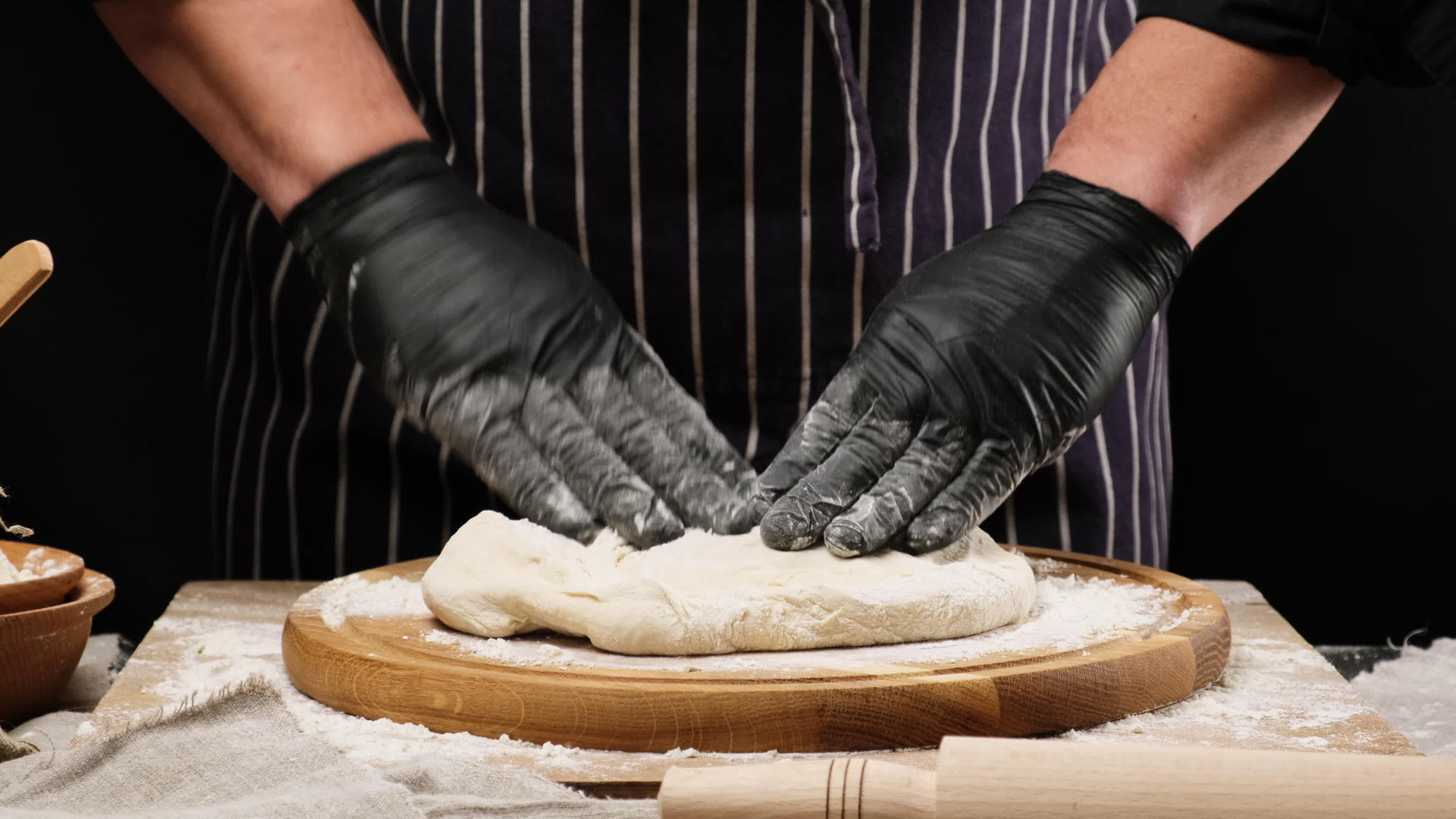 黑色乳头厨师用黑色面粉手套在圆木板上的白色小麦面粉面团上视频的预览图