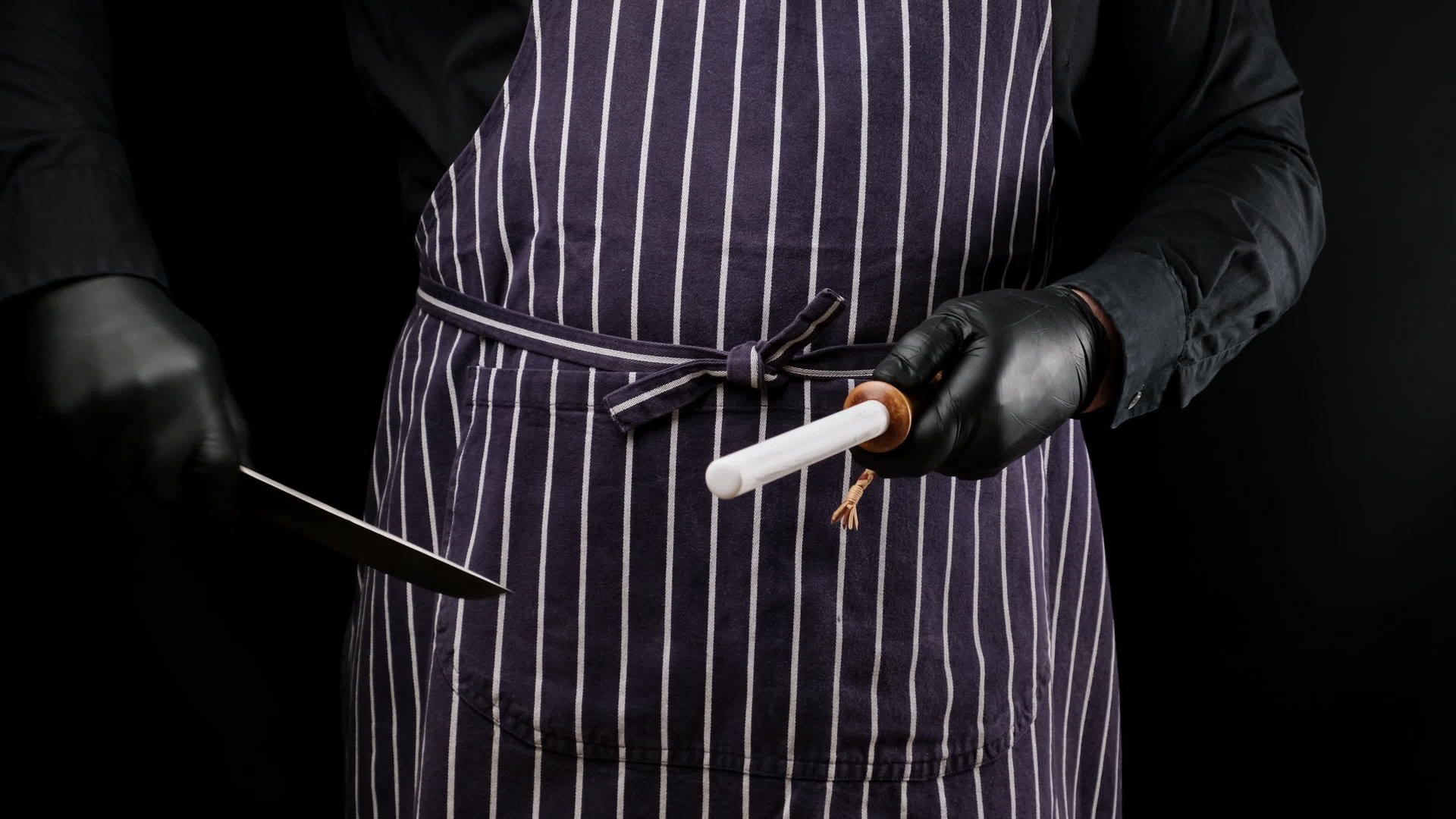 厨师使用黑色乳胶手套和条纹围裙黑色木柄黑色背景视频的预览图