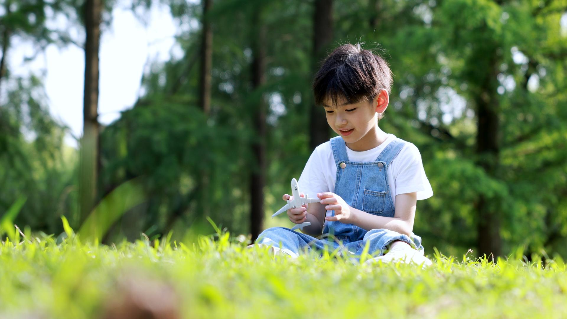 小男孩坐在草地上玩小飞机玩具视频的预览图