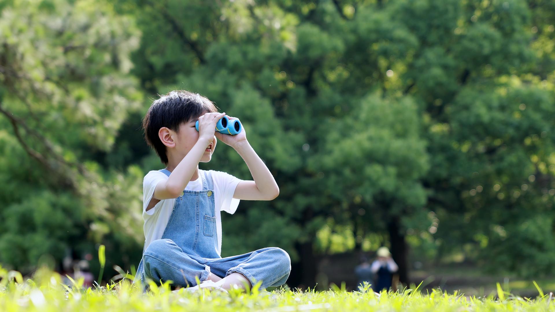 小男孩坐在草地上拿望远镜望向远方视频的预览图