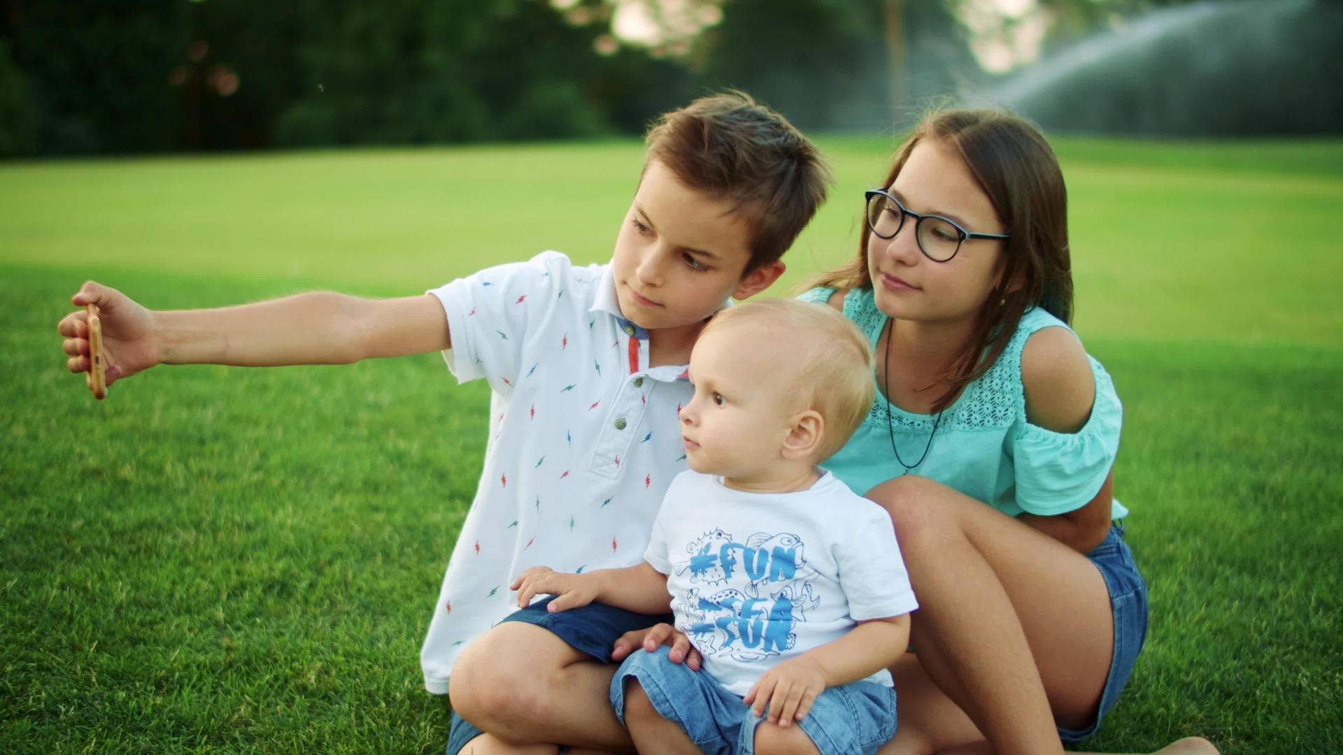 微笑的男孩和女孩坐在绿色的草地上自拍视频的预览图