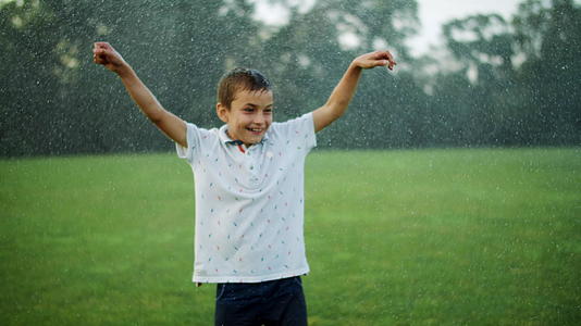 快乐的男孩坐在草地上被喷水器弄湿了视频的预览图