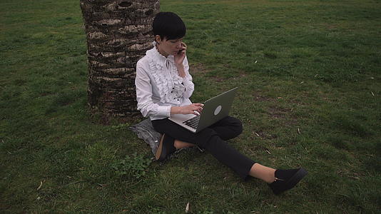 女性坐在公园的树下工作视频的预览图