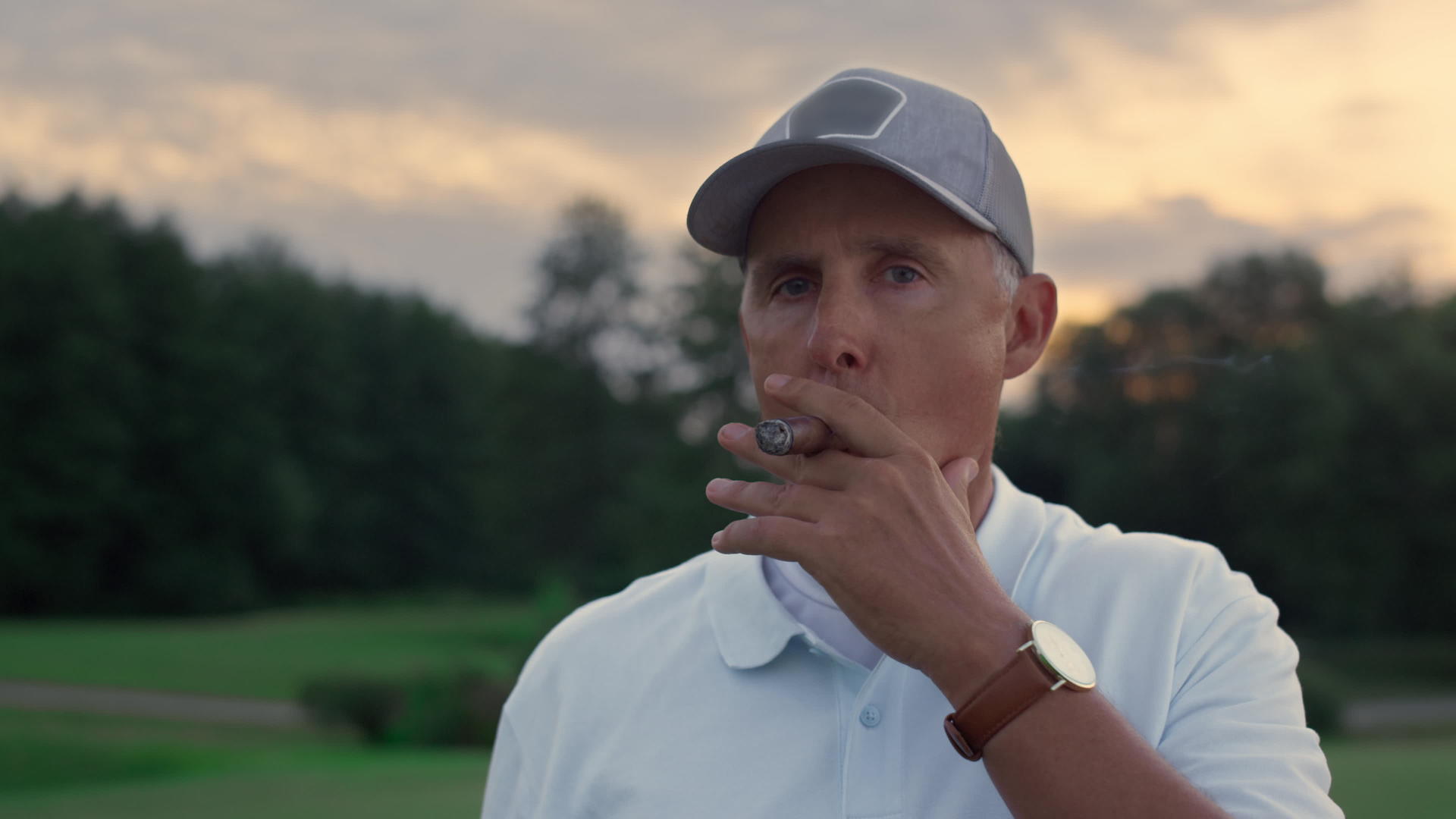 高级高尔夫球手在日落球场球道上抽雪茄看相机视频的预览图