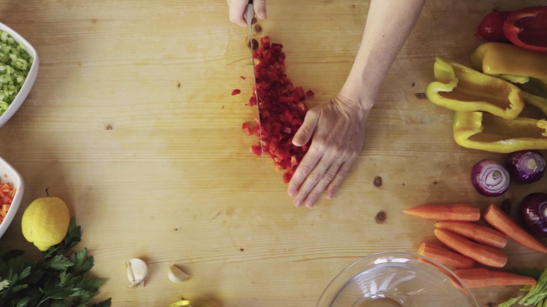 平躺的顶视镜头是一个女人的手在她的轻木工作桌上切红辣椒视频的预览图