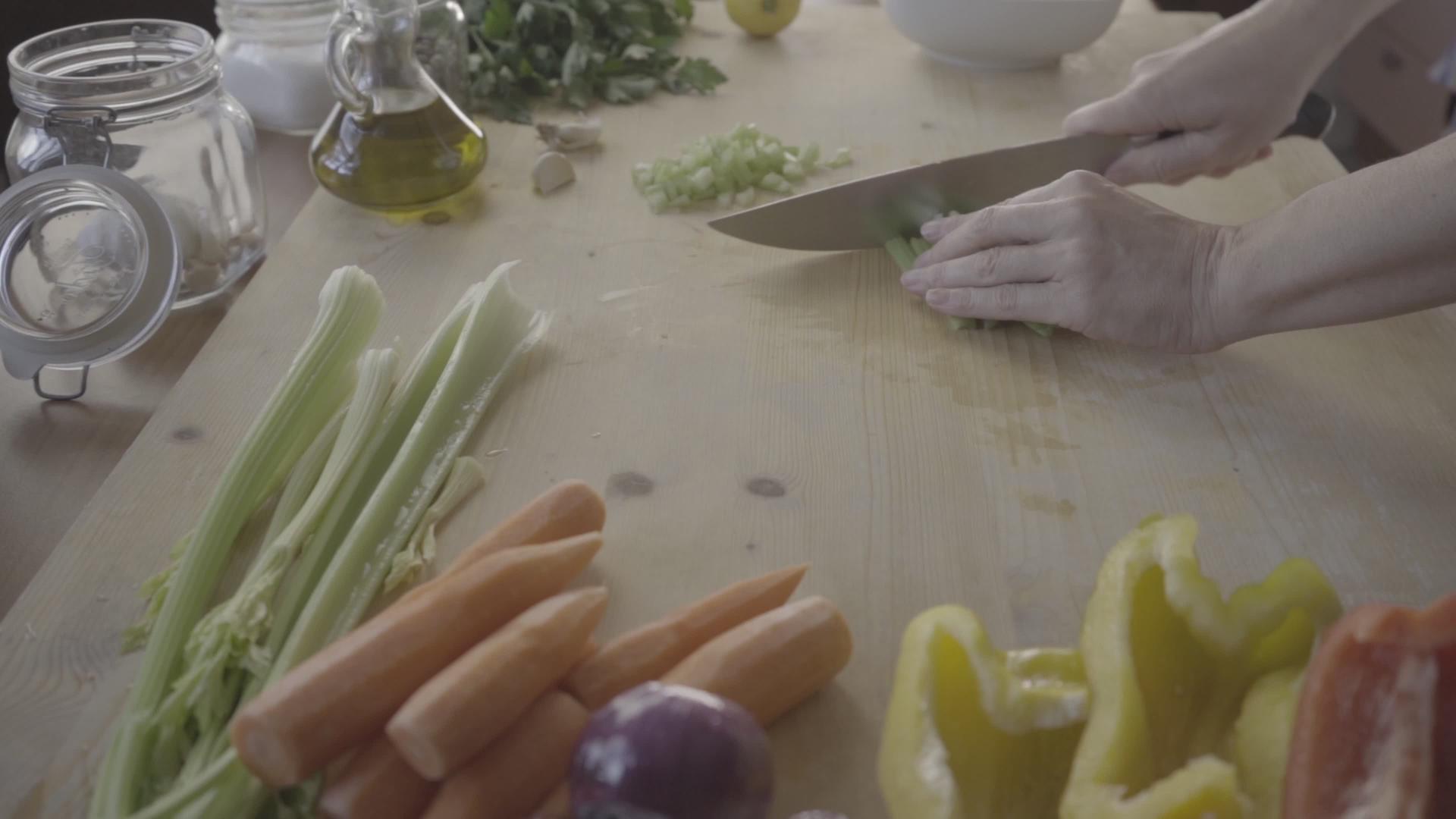 一位年轻的女厨师在家庭烹饪的浅色木制工作台上切芹菜视频的预览图