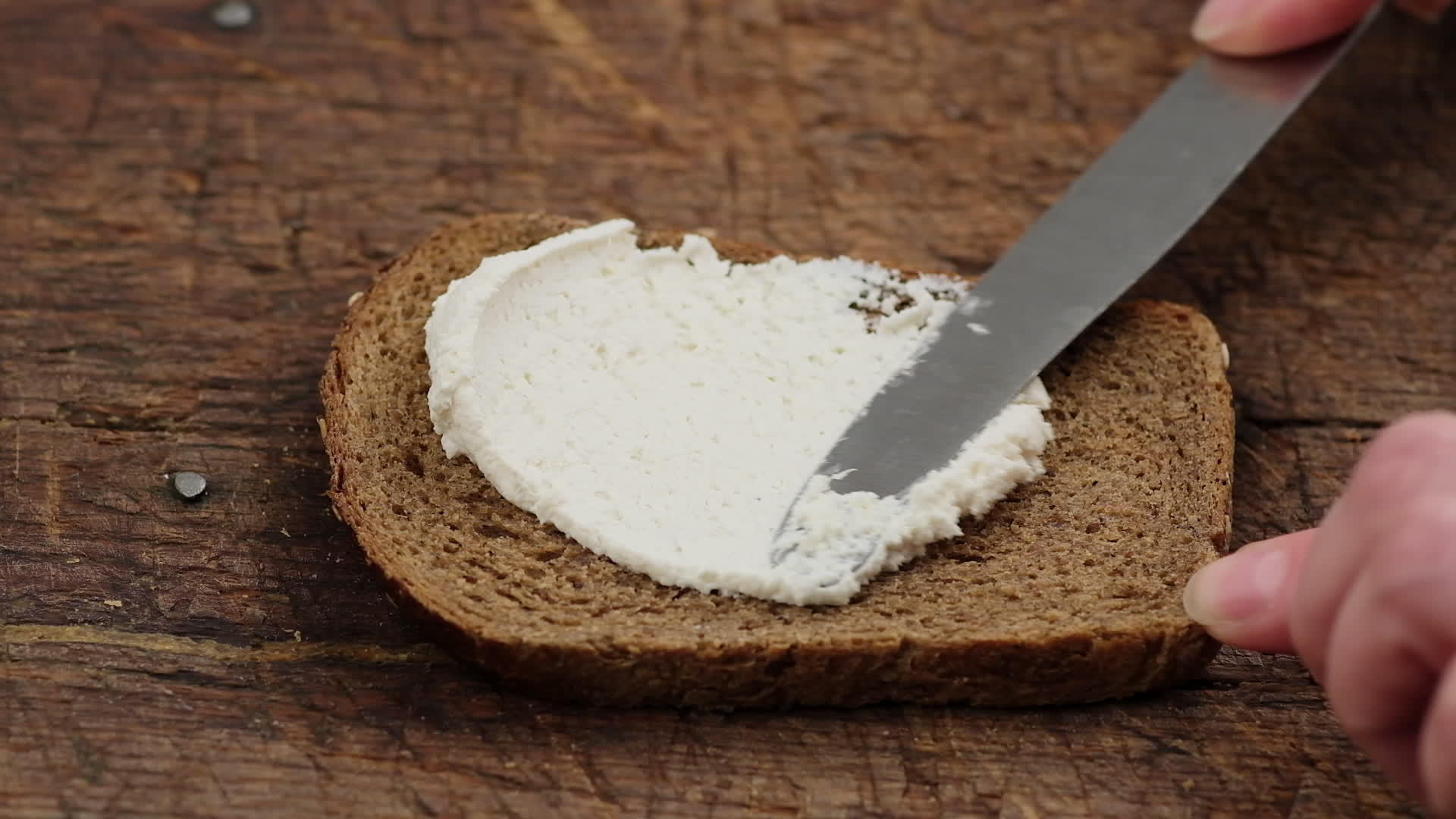 手里拿着一把刀把白奶酪撒在烤面包上的黑麦面包上视频的预览图