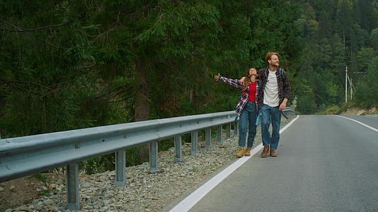 兴奋的旅行者在山路上搭便车视频的预览图