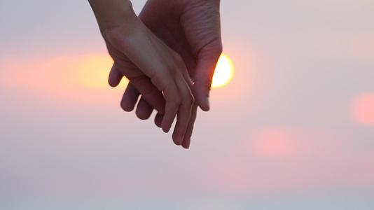 关闭两个情人手牵手男人和女人手牵手日落模糊背景视频的预览图