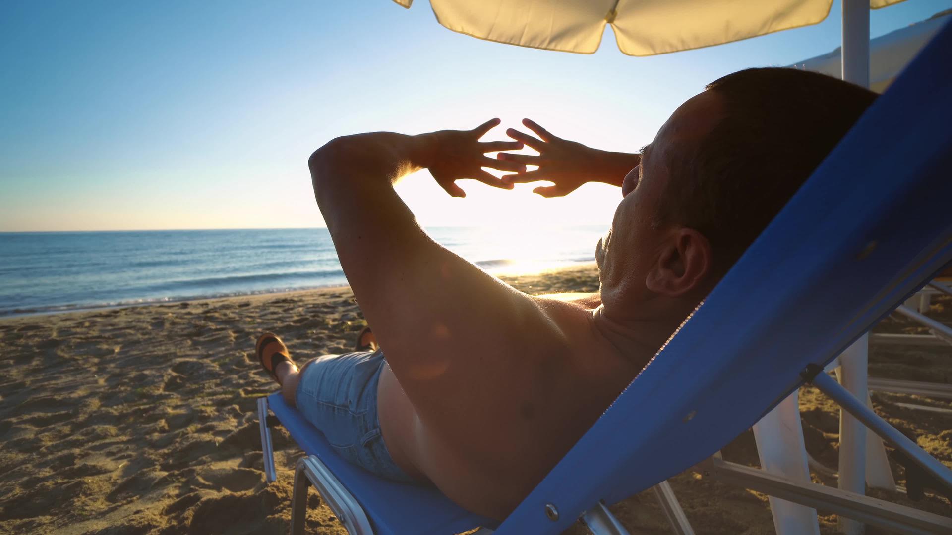 男人在日落的天空中用双手玩太阳躺在海滩上他们的精神幸福是积极的视频的预览图