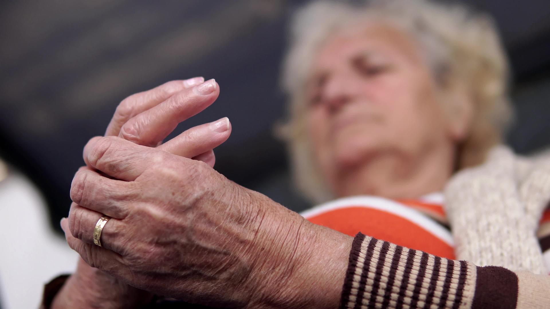 老妇人坐在户外门廊的秋千椅上在疼痛的手上做理疗康复按摩疗法视频的预览图