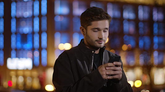 冷静的男人在黑暗的街道上给手机发短信放松的家伙玩智能手机视频的预览图