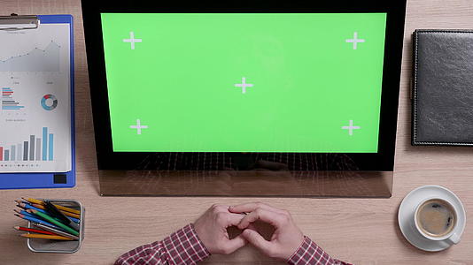 一名男子看着上面的显示屏和绿色屏幕视频的预览图