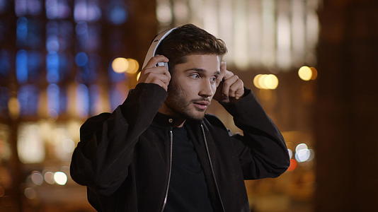 在街上通过耳机听音乐的帅哥视频的预览图