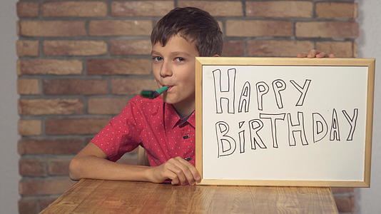 坐在桌旁的孩子拿着翻页的照片在红砖墙上写着生日快乐视频的预览图
