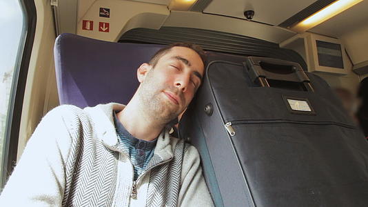 年轻人在火车上旅行睡在他旁边的蓝色手提箱里视频的预览图