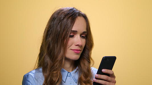 女性在黄色背景下使用智能手机视频的预览图